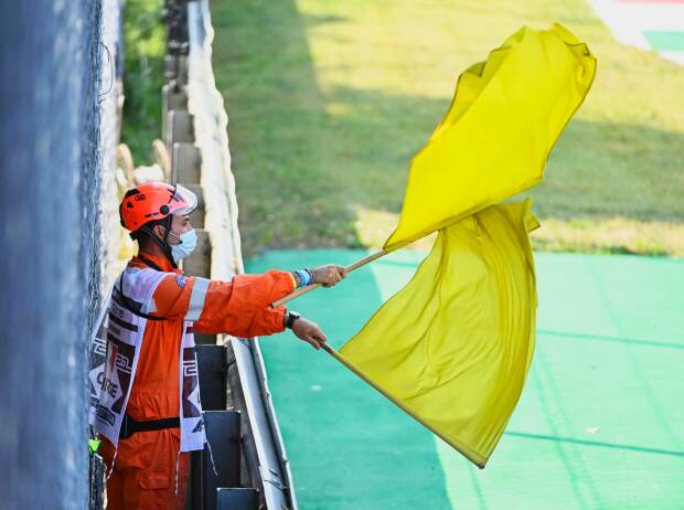 Ein Formel-1-Marshall schwenkt doppelt gelbe Flaggen Ein Formel-1-Marshall schwenkt doppelt gelbe Flaggen